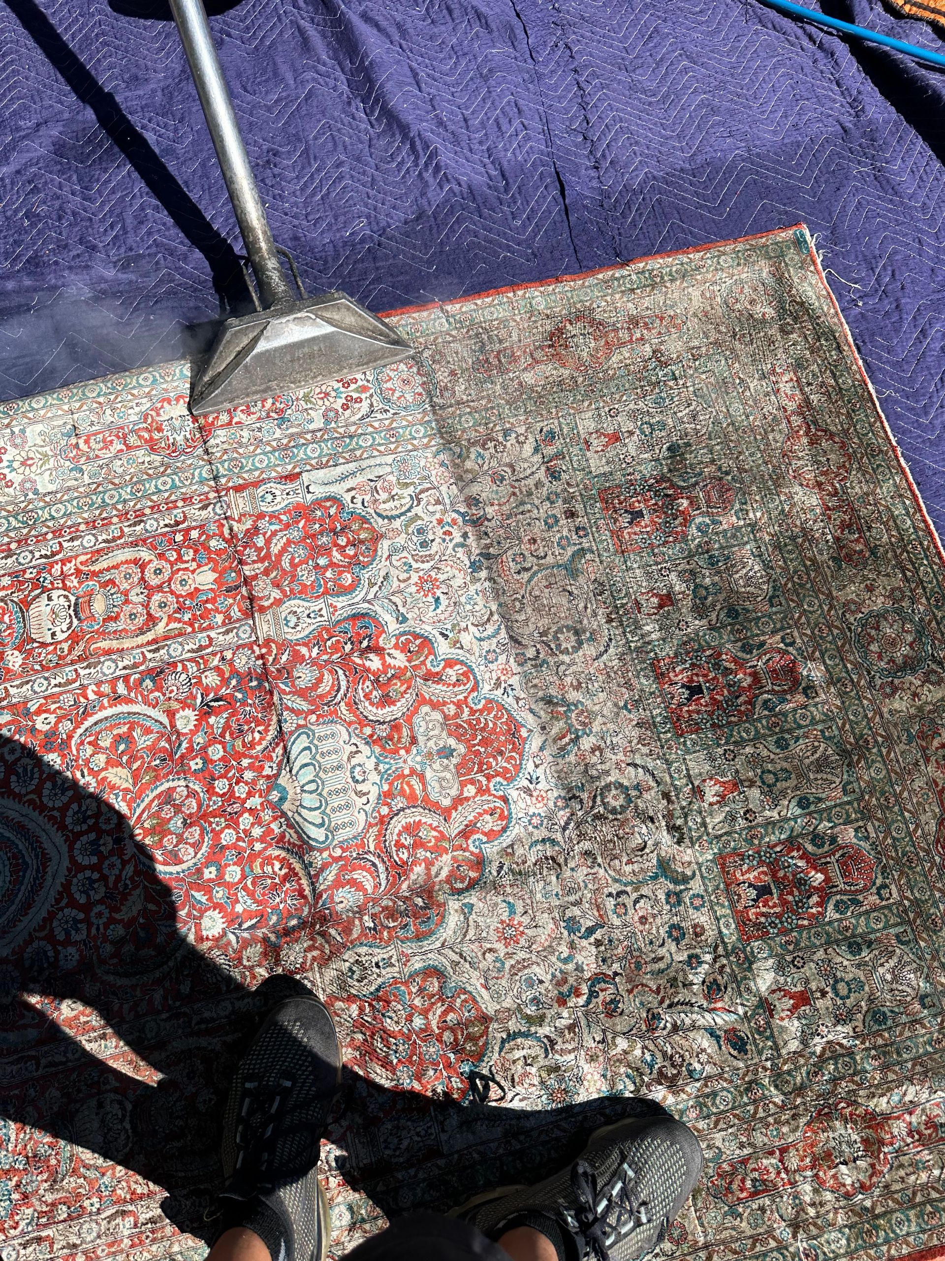 Feet on a red and gray patterned rug beside a metal chair leg and shadow.