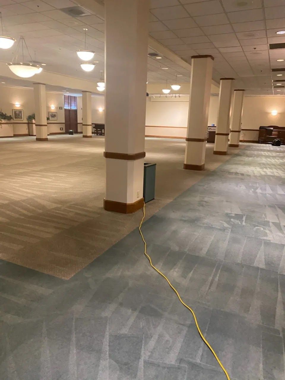 Empty banquet hall with white columns, tan carpet, and a yellow cord across the floor