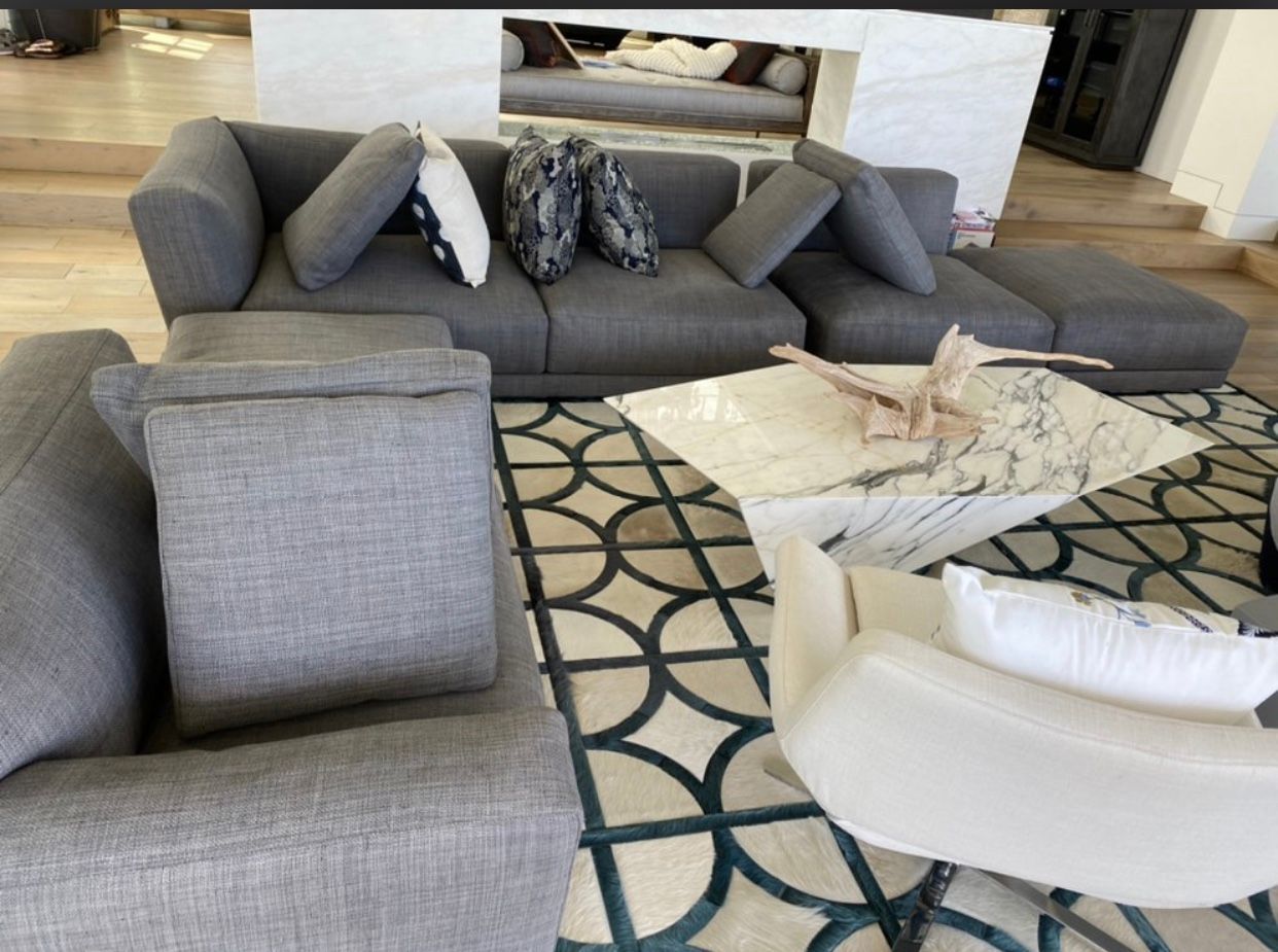 Modern living room with gray sofa, patterned rug, and cream chairs around a coffee table.
