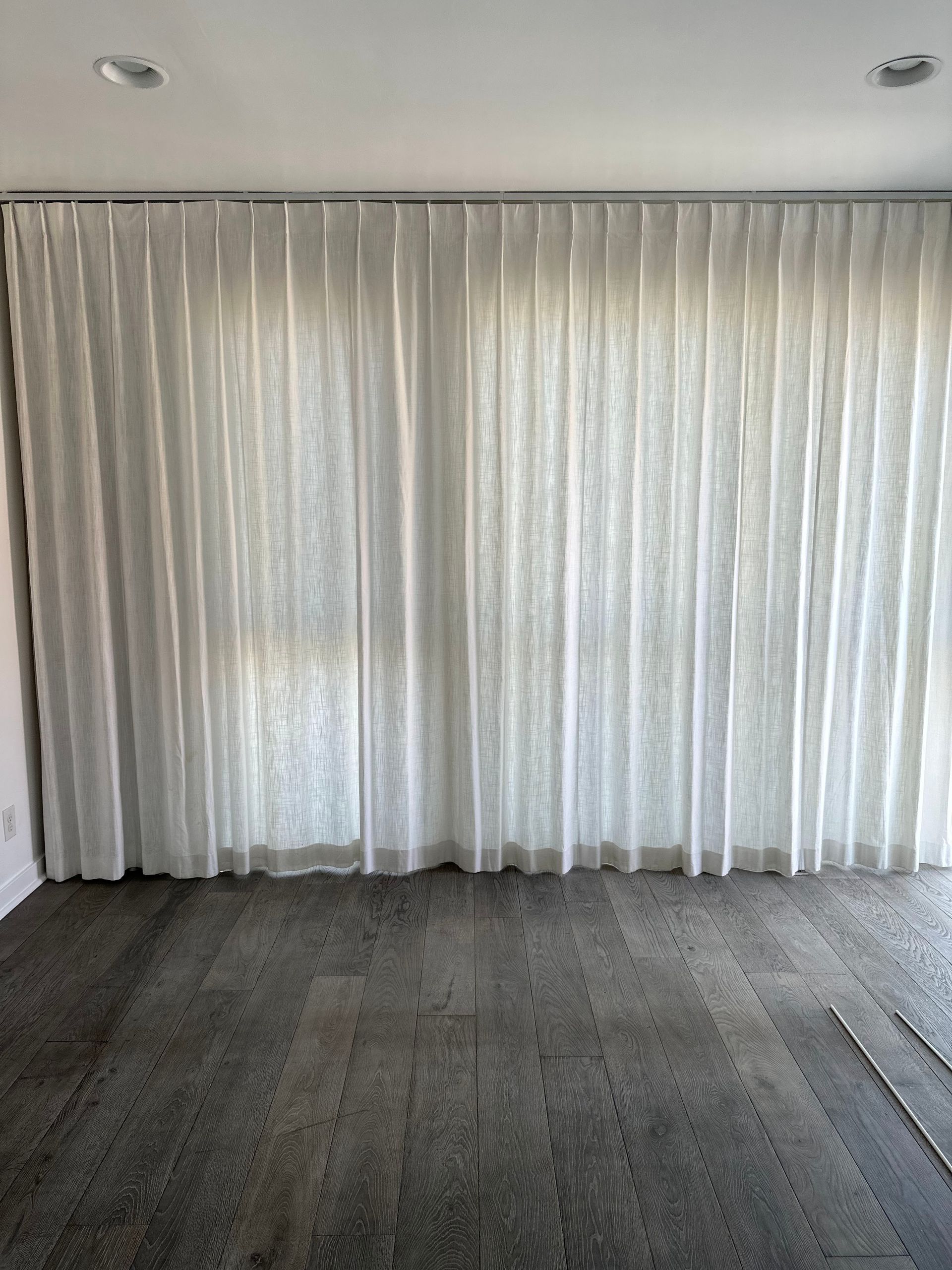 Empty room with sheer white curtains, gray wood floor, and recessed ceiling lights