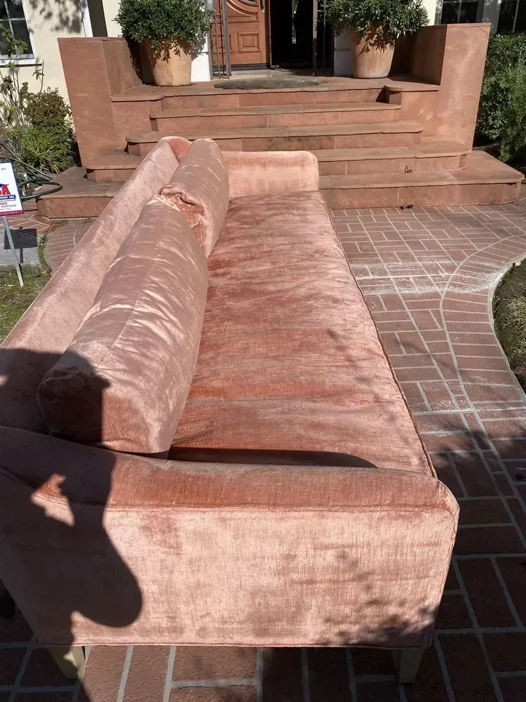 Pink upholstered couch on a brick patio in front of steps and potted plants