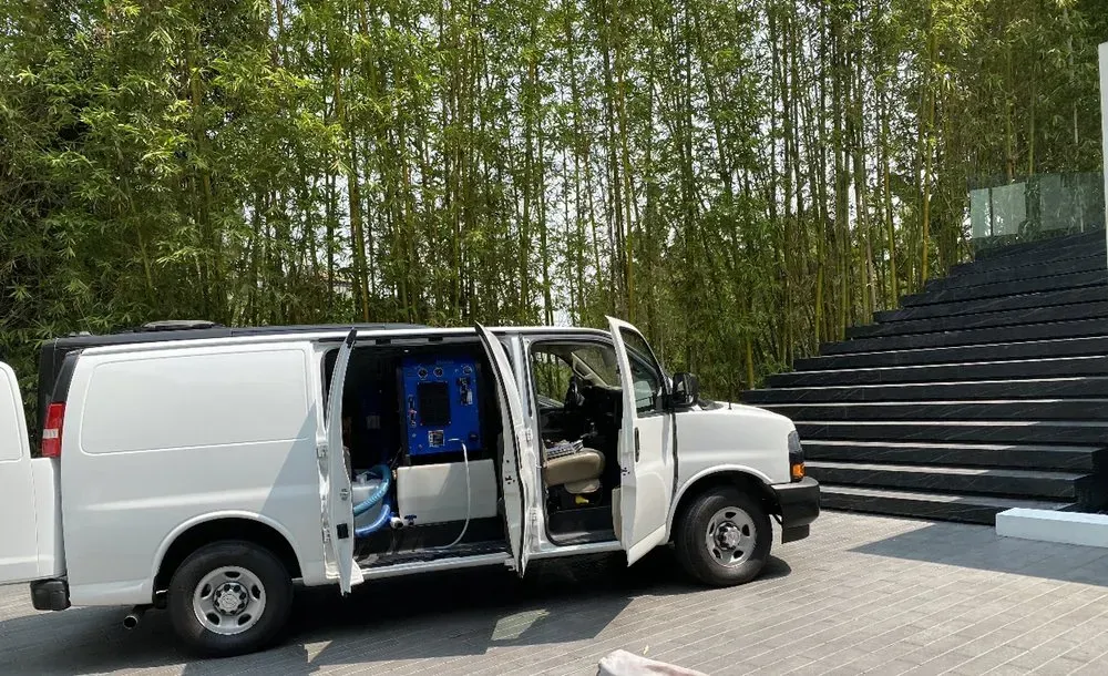White cargo van parked beside outdoor steps, side doors open in a wooded area