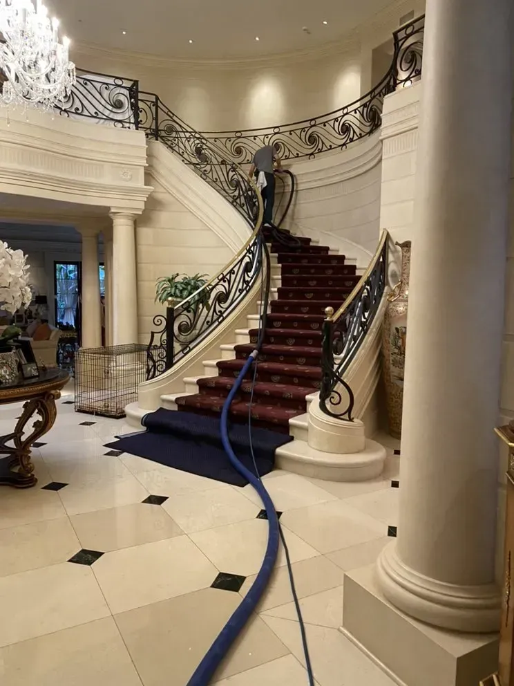 Grand staircase with red carpet and ornate wrought-iron railing in a grand foyer, blue hose across the floor