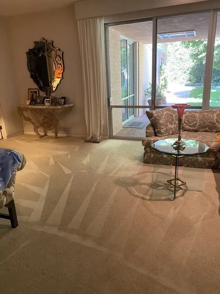 Elegant living room with beige carpet, ornate mirror, console table, and glass coffee table by sliding doors.