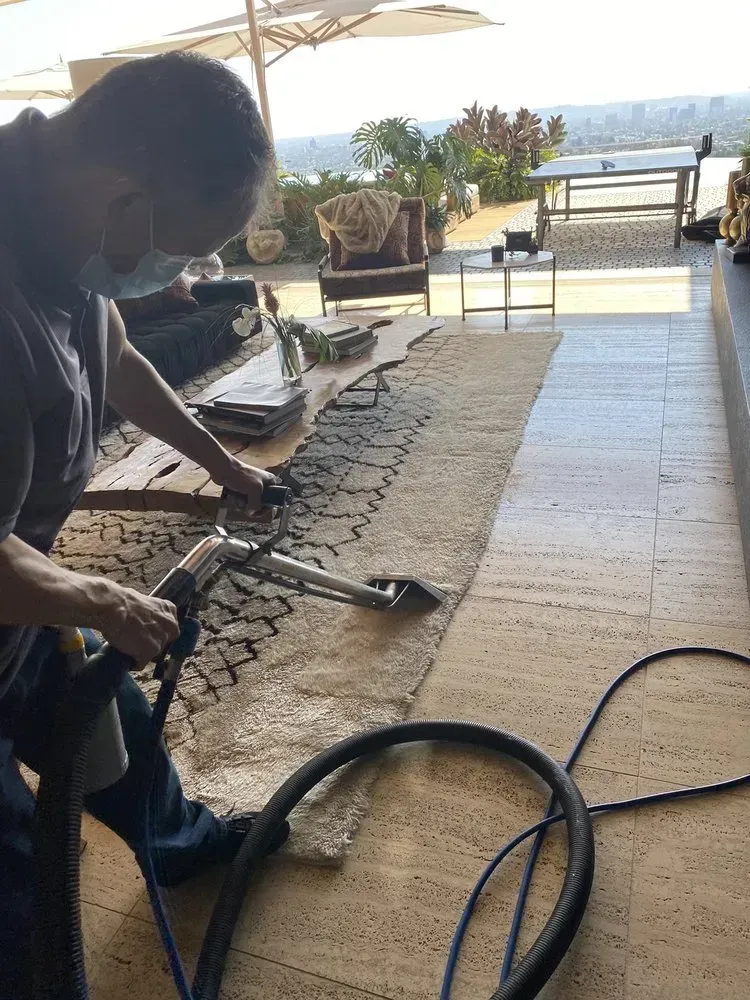 Person vacuuming a patio with ocean view and outdoor furniture in the background