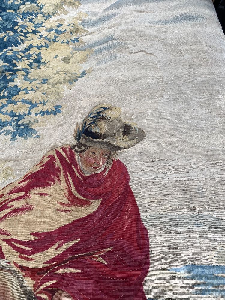 Person in a red cloak and wide-brimmed hat standing outdoors near a flowering tree and cloudy sky
