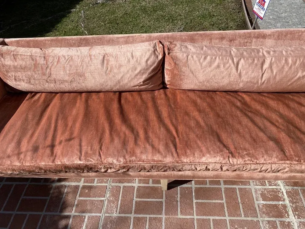 Brown outdoor sofa with two cushions on a brick patio, set against a grass lawn.