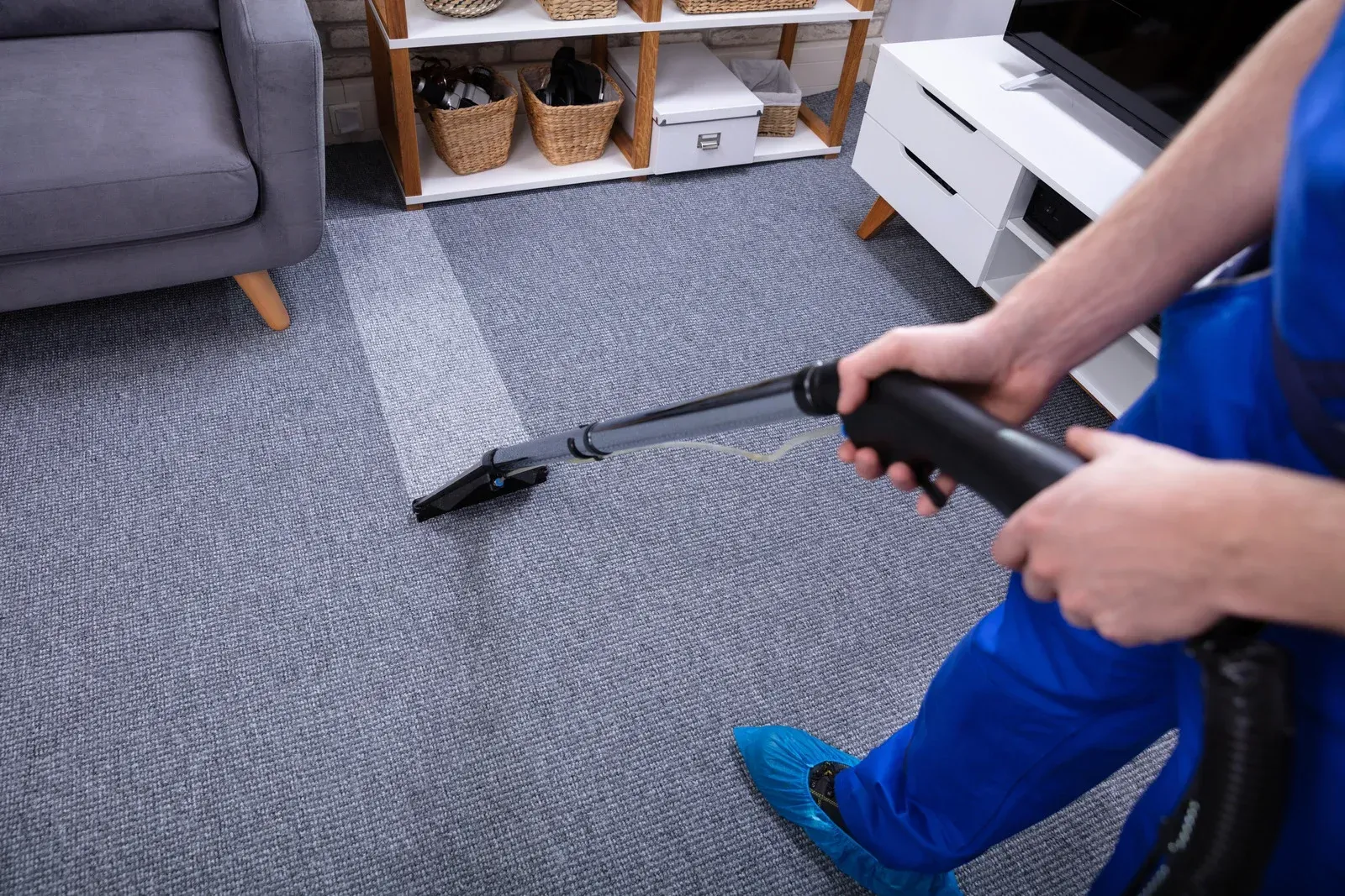 Person vacuuming a gray carpet in a living room with a sofa and white TV stand