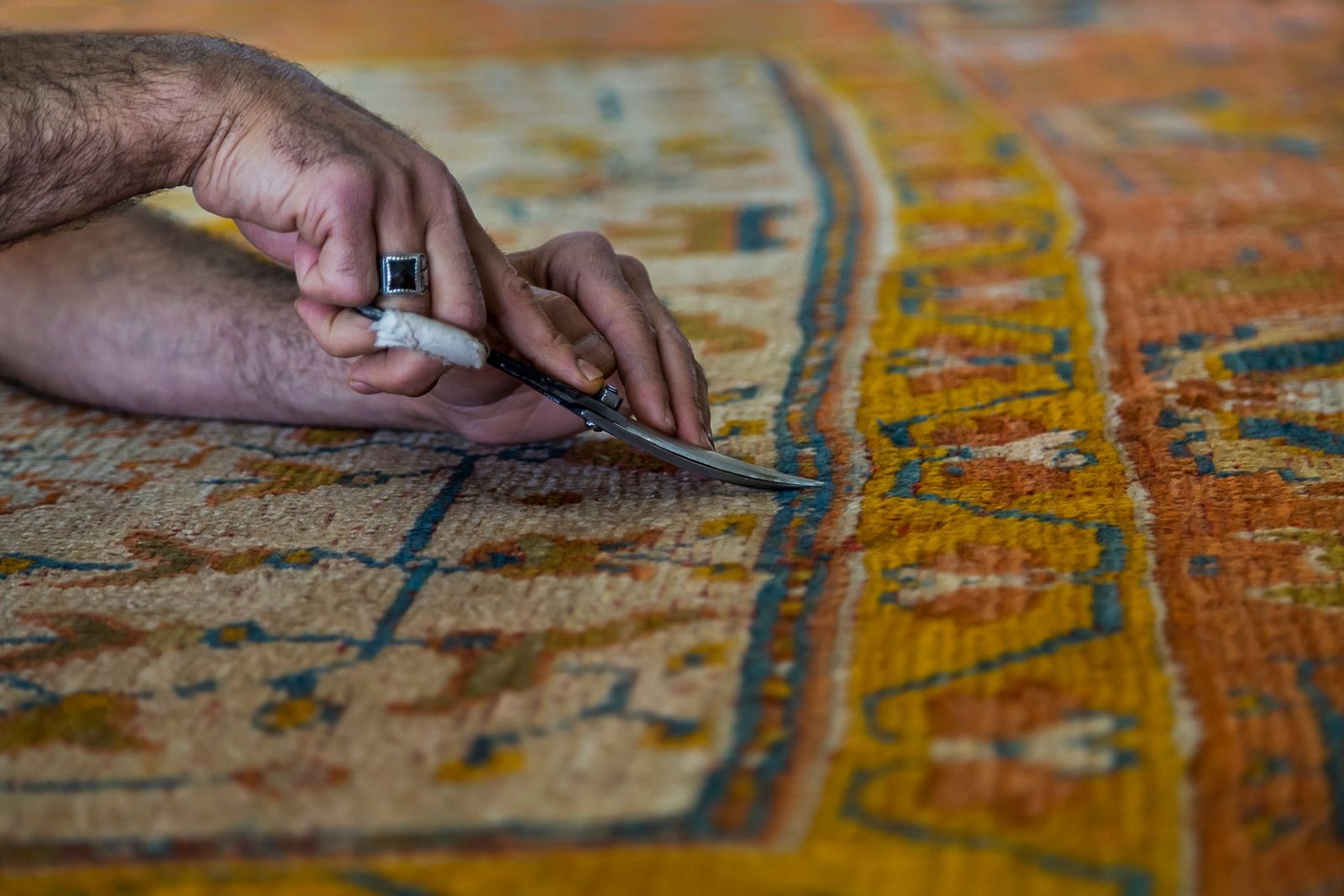 Hand using scissors to cut a colorful woven rug with orange and blue patterns