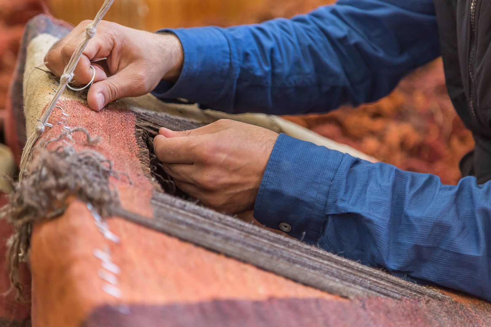 Hands hand-stitching a brown leather saddle with blue sleeves visible