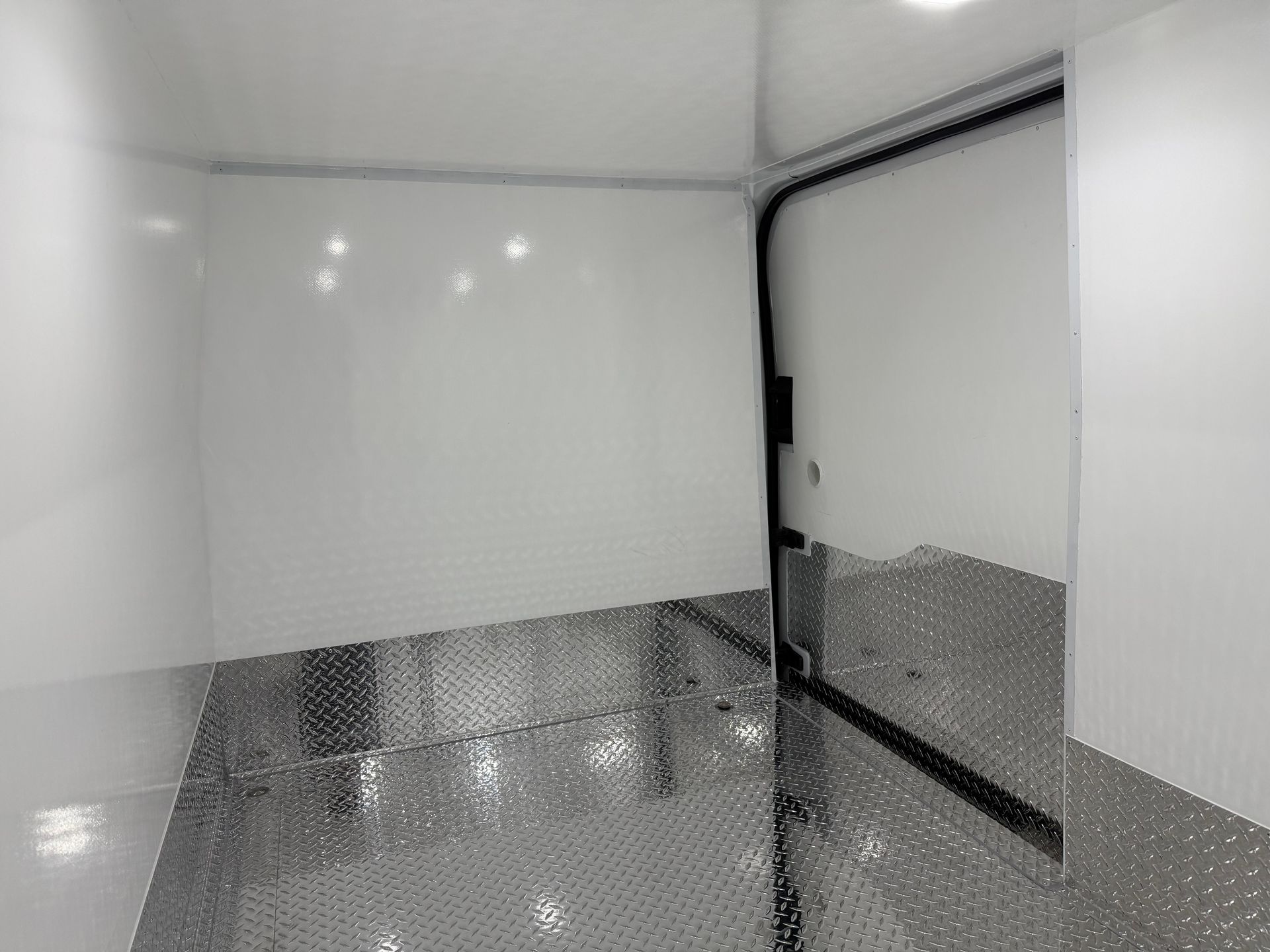 Interior of an empty trailer with white walls and a reflective, metallic diamond plate floor leading to an open doorway.