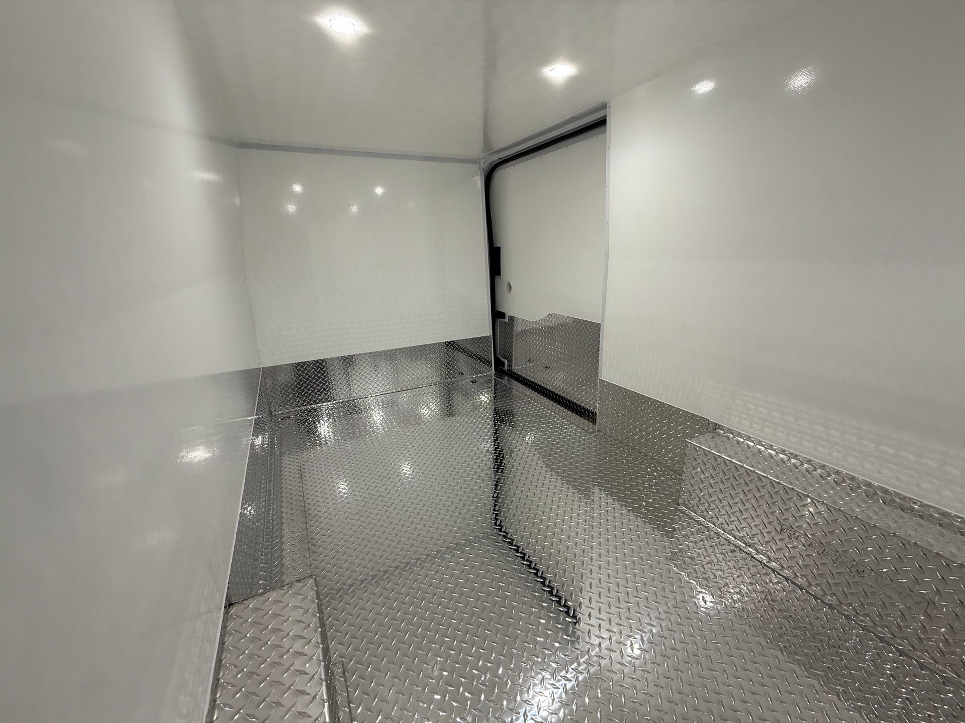 Interior of a clean trailer with smooth white walls, recessed ceiling lights, and diamond-plate metal flooring.