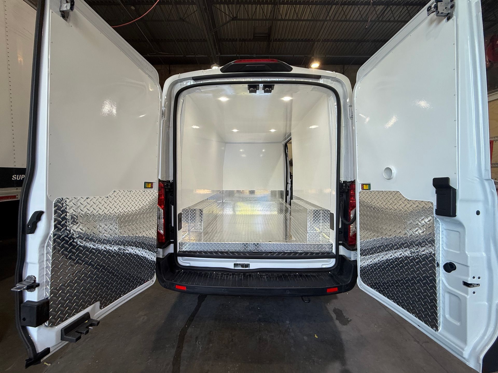 The rear view of a white van with its double doors open, revealing a clean, empty cargo space with diamond-plate lining.