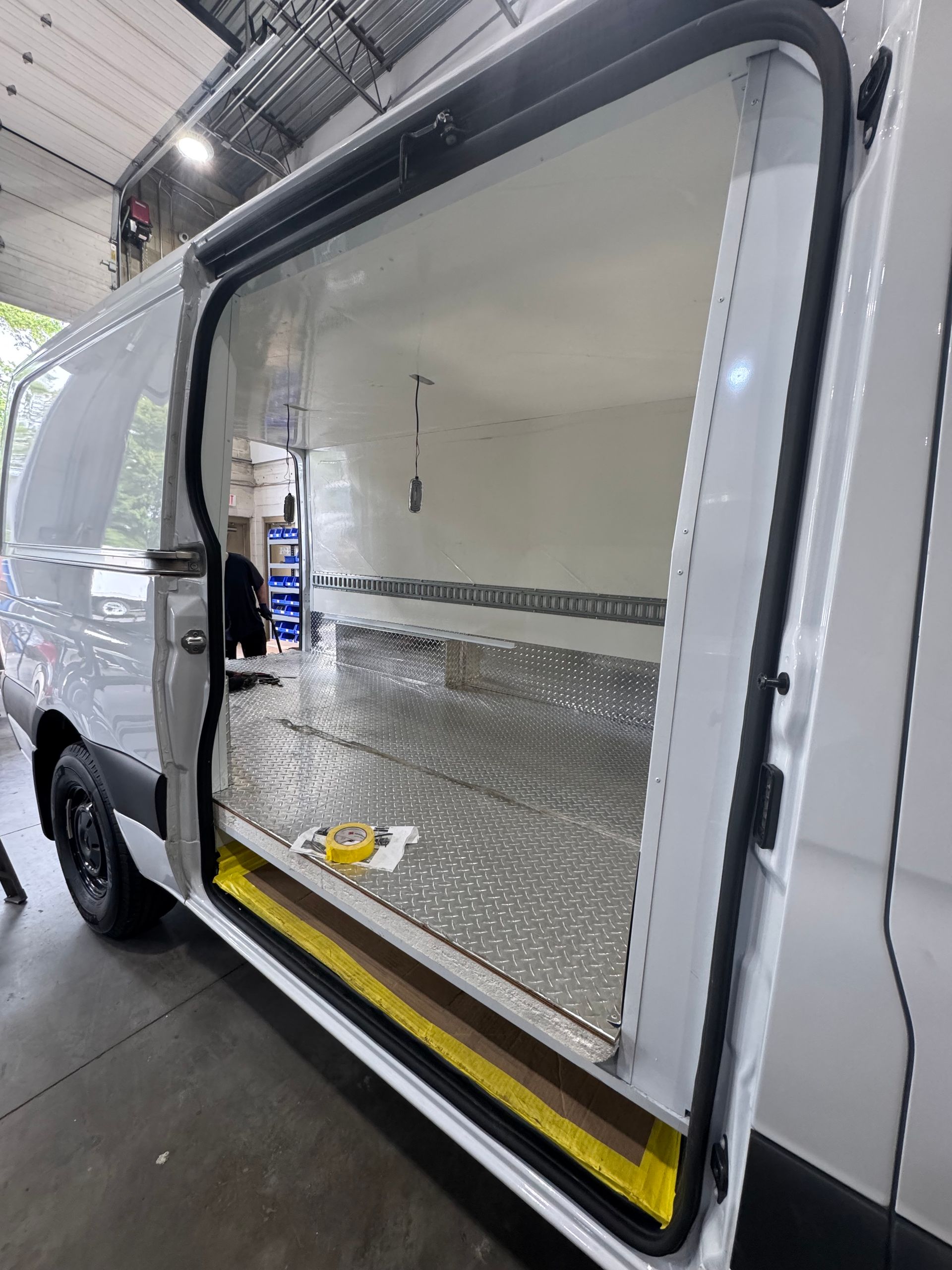 The open sliding door of a white commercial van shows a clean cargo area with diamond-plate flooring and wall trim.