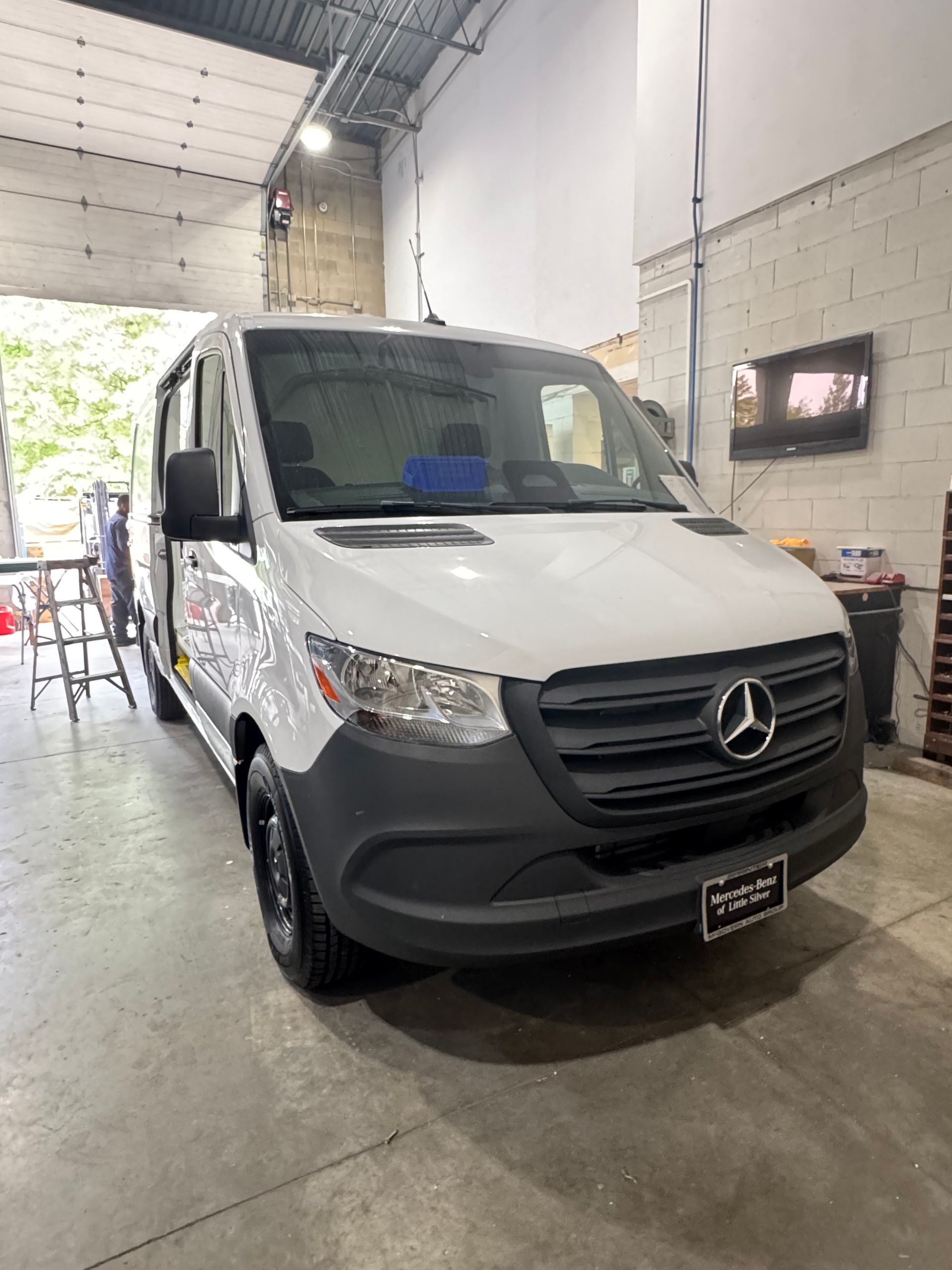 A white Mercedes-Benz Sprinter van parked inside an industrial garage with a concrete floor.
