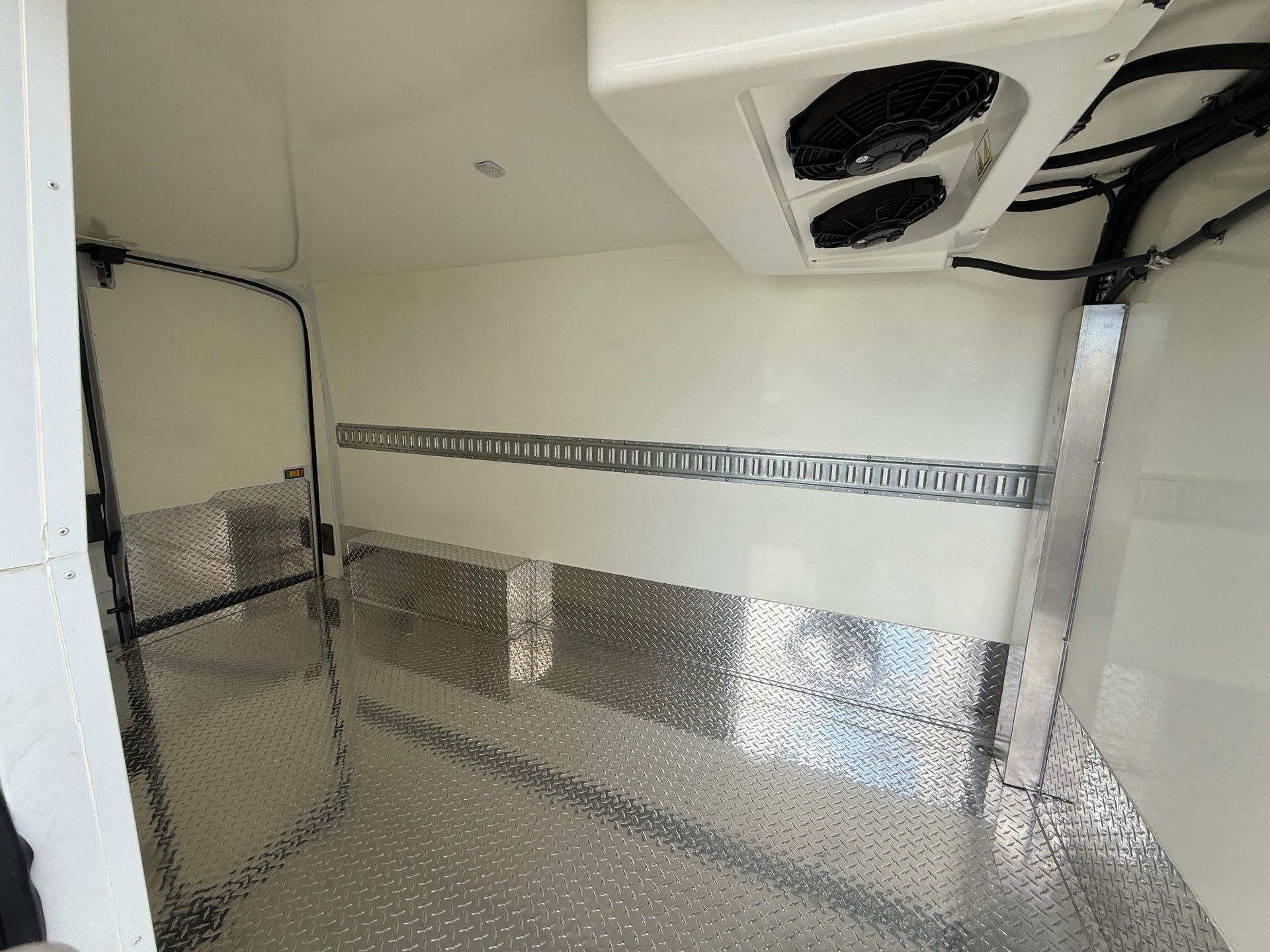 Interior of a refrigerated cargo trailer with white walls, diamond plate metal flooring, and horizontal cargo tracks.