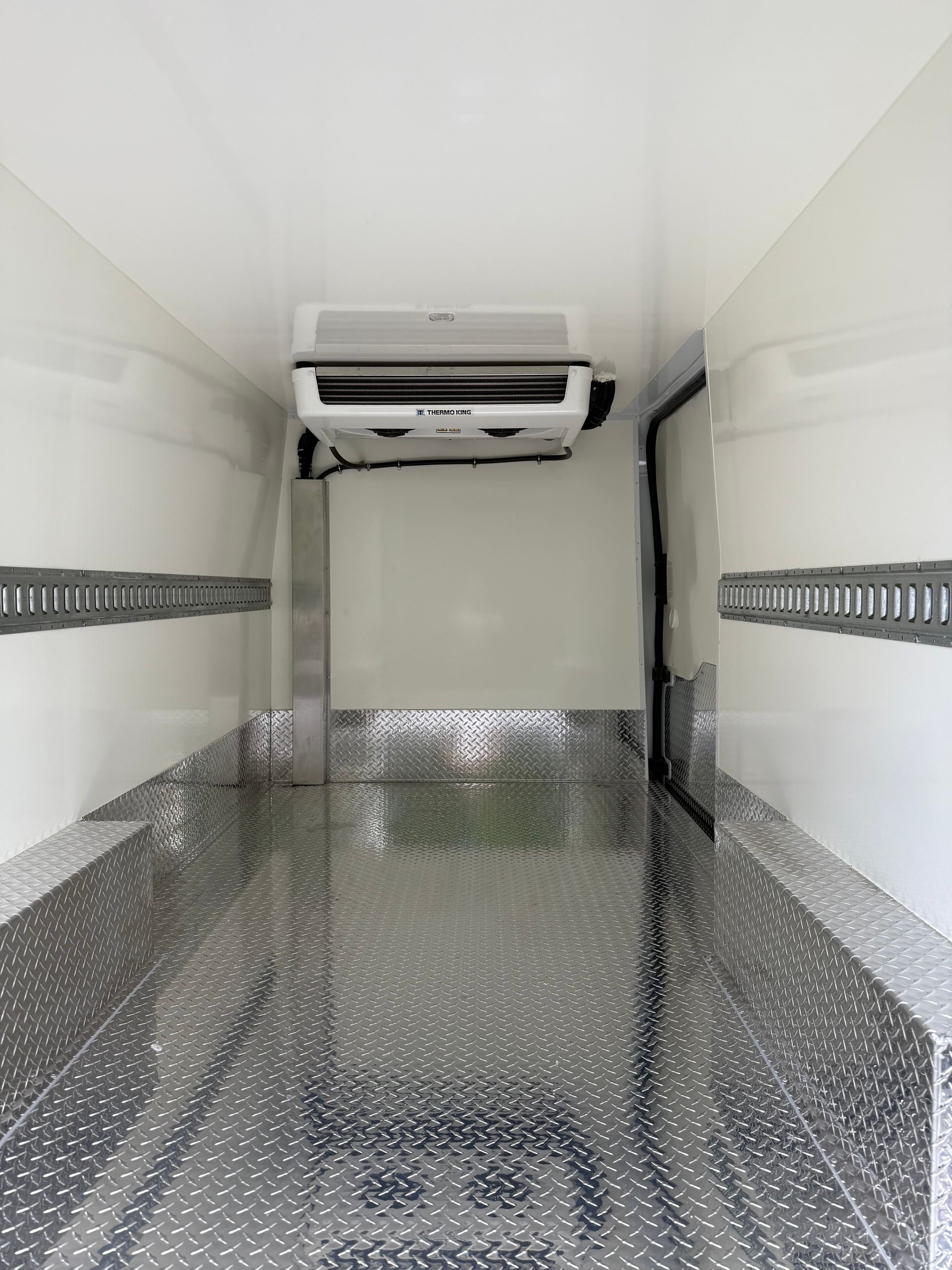 The interior of a refrigerated delivery van with diamond-plate metal flooring and a cooling unit mounted on the ceiling.