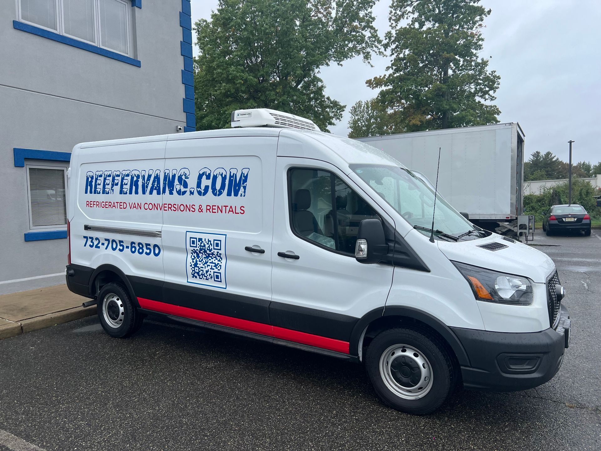 A white ReeferVans.com refrigerated cargo van parked outside a building on an overcast day.