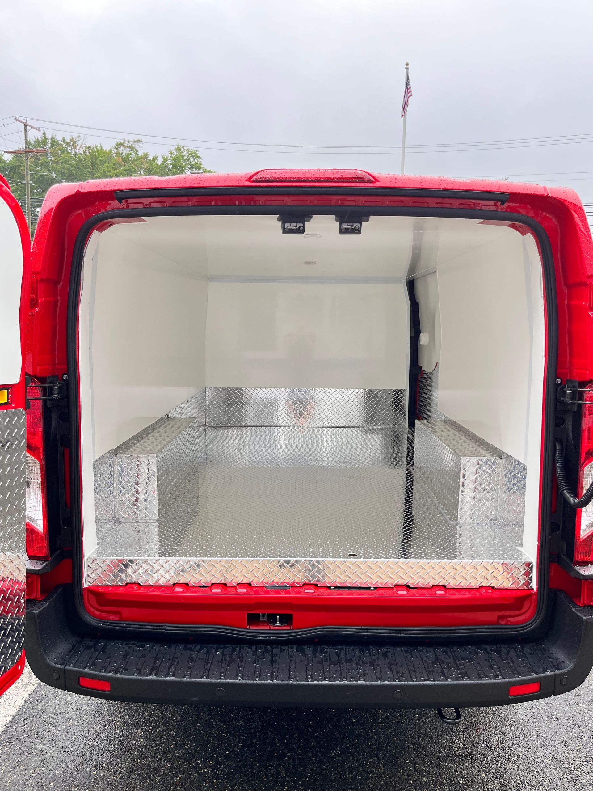 The open rear doors of a red cargo van, showing an empty, clean interior with metallic diamond-plate floor panels.