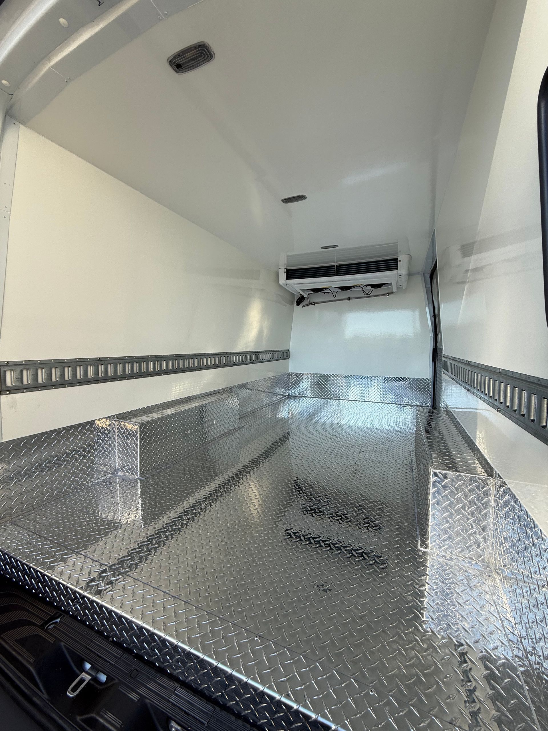 Empty cargo area of a refrigerated van with white walls, diamond plate flooring, and logistics tracks on the sides.