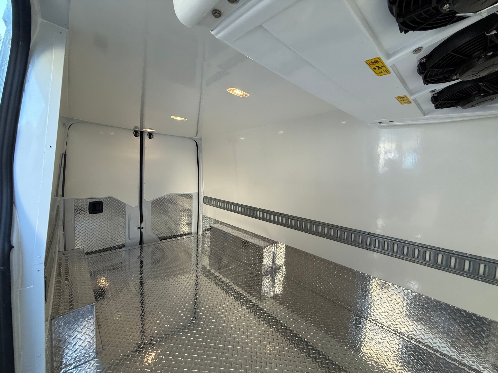 Empty, clean white interior of a refrigerated cargo van featuring diamond-plate flooring and side wall tracking.