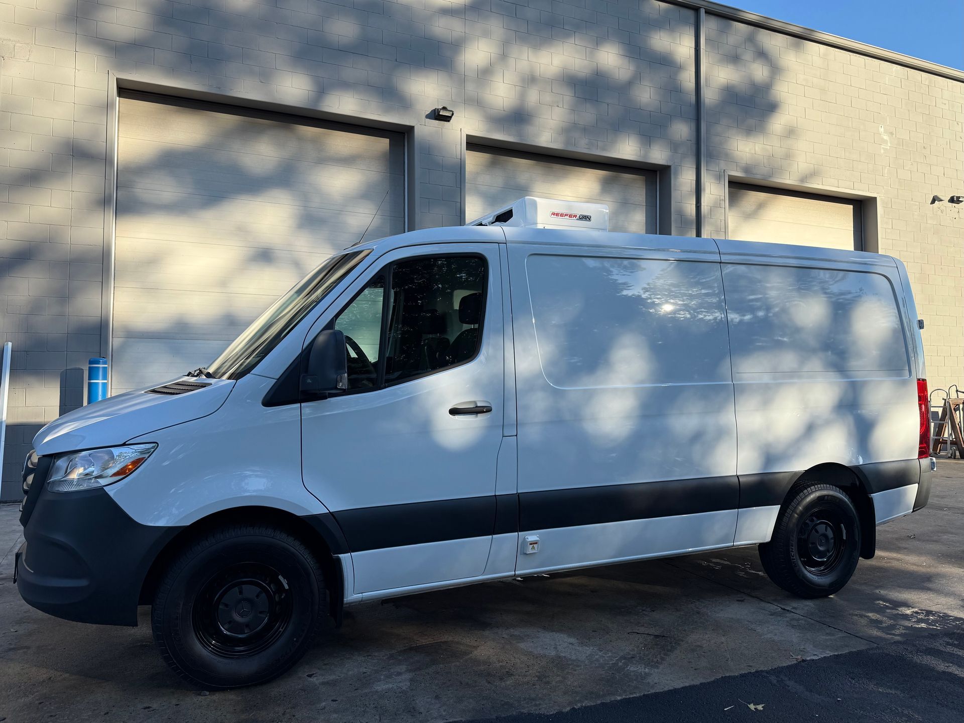 A white Mercedes-Benz Sprinter cargo van parked in front of a building with three garage doors.