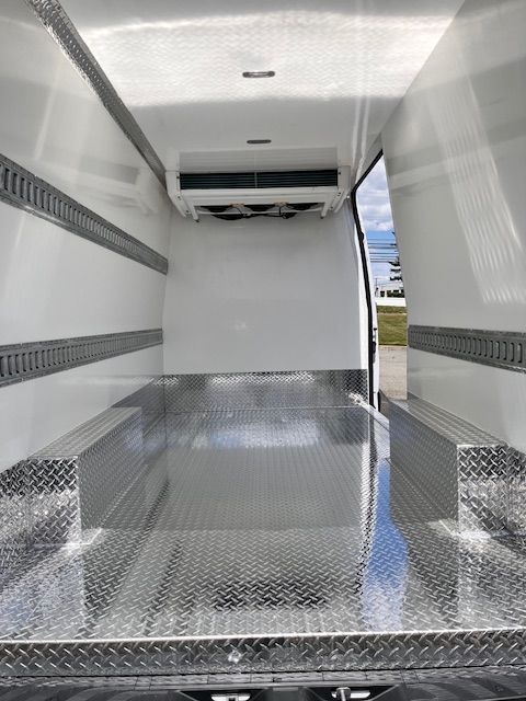 Interior of a refrigerated van with white walls, metal diamond-plate flooring, and e-track cargo rails on the sides.