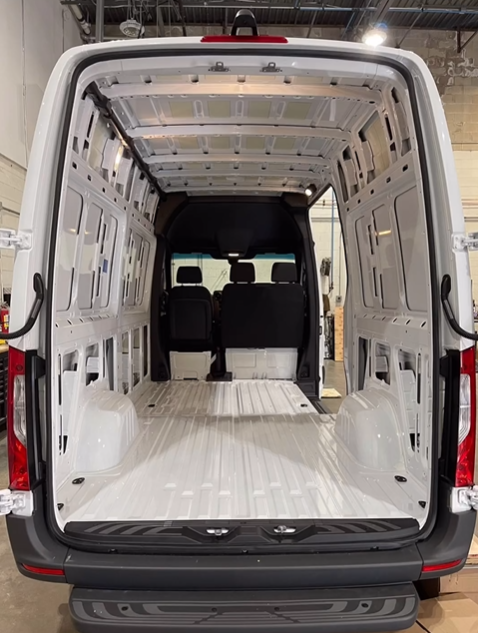 Empty, white interior of a commercial cargo van, showing the floor, side walls, and view into the driver's cabin.