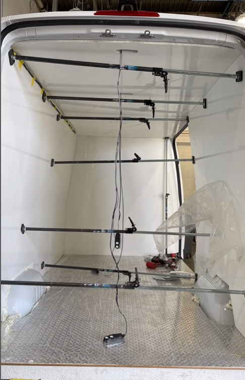Interior of an empty white van cargo space with several horizontal metal cargo bars installed across the width.