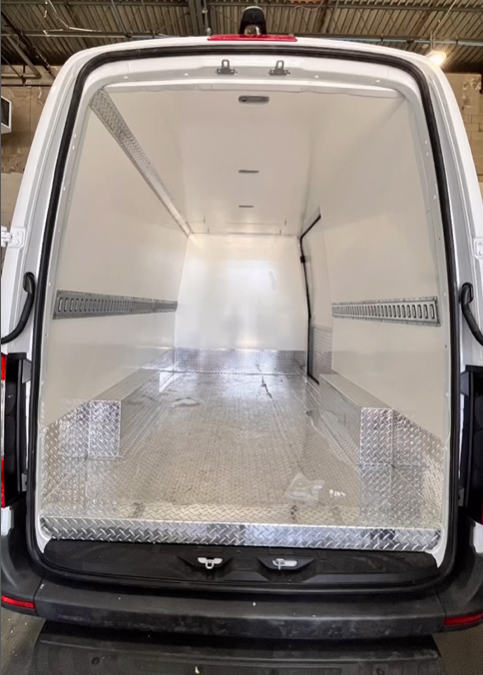The empty interior of a cargo van with white walls, a diamond-plate metal floor, and horizontal cargo tracks.