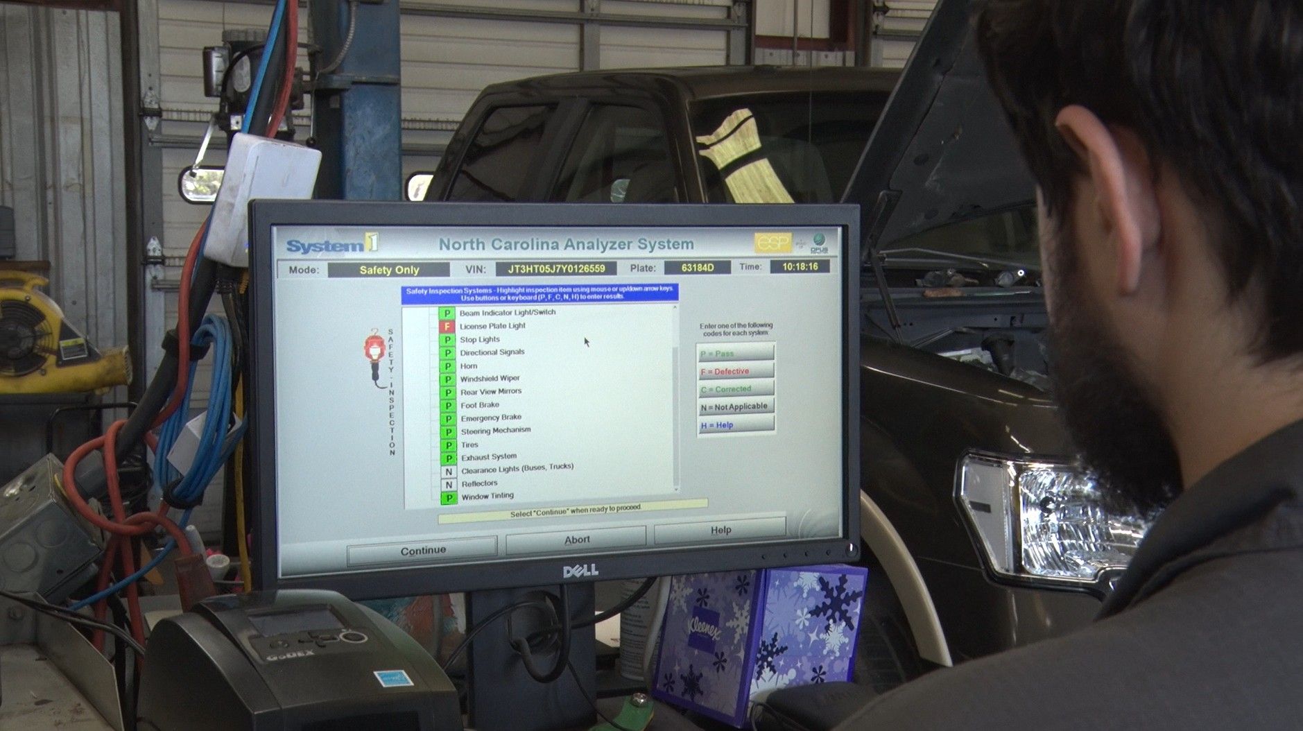 Mechanic viewing a diagnostic computer screen beside a car in a garage