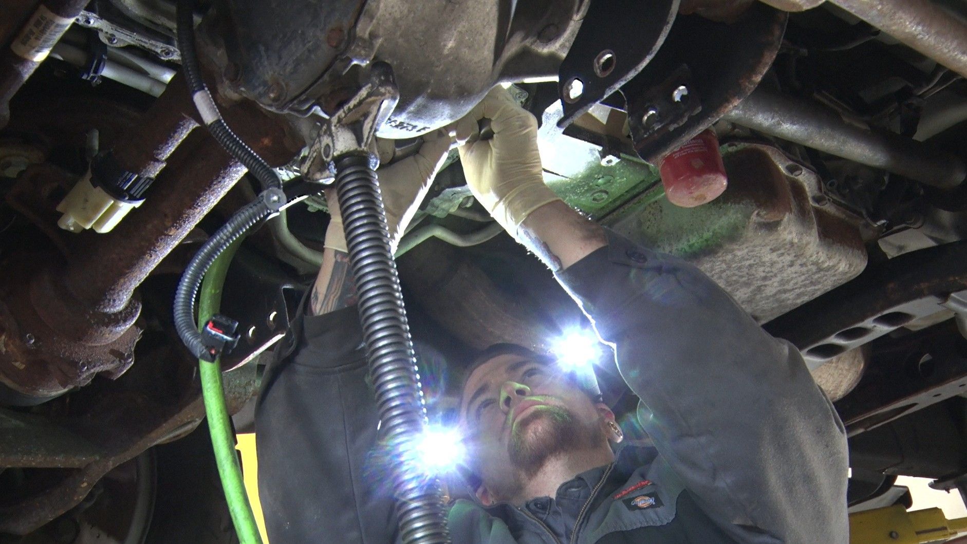 Worker in hard hat using a flashlight to inspect machinery in a dark engine compartment.