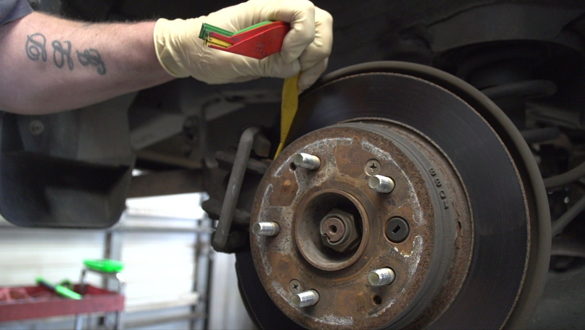 Mechanic’s gloved hand measuring brake rotor thickness on a car wheel hub with caliper