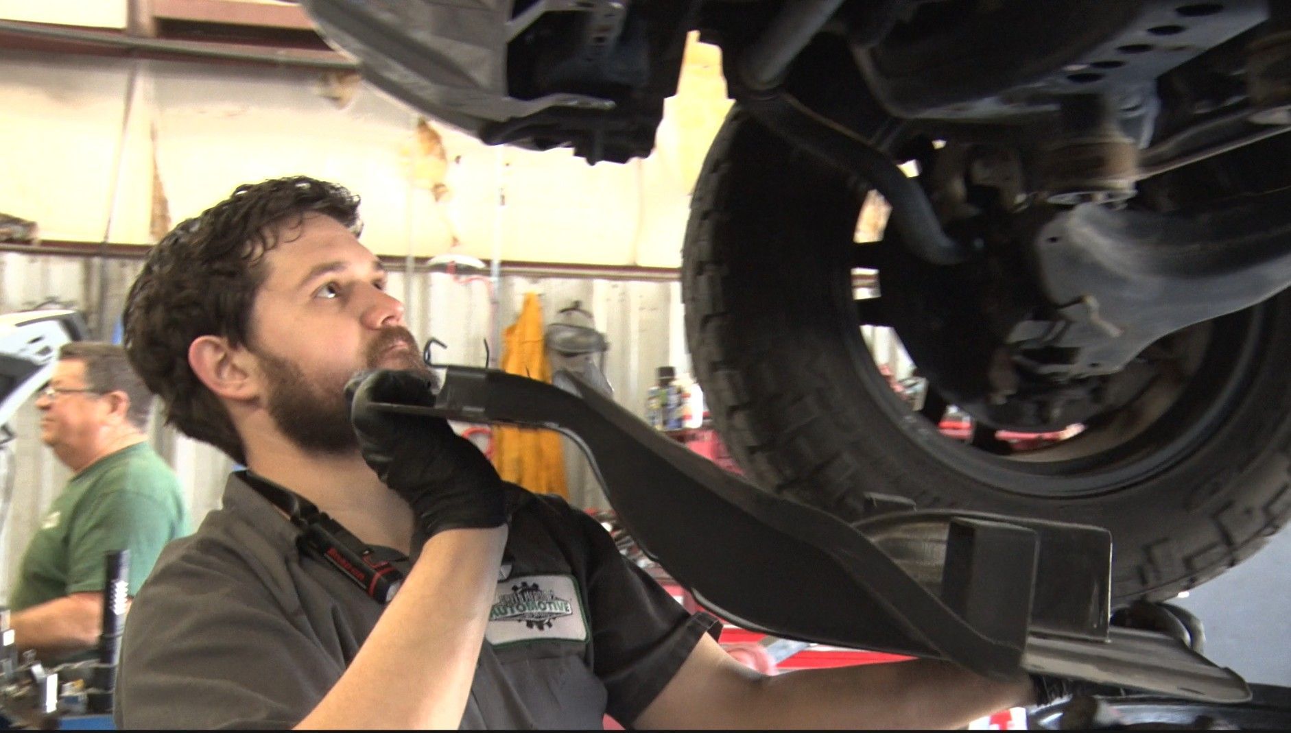 Mechanic inspecting the underside of a car on a lift in an auto repair shop