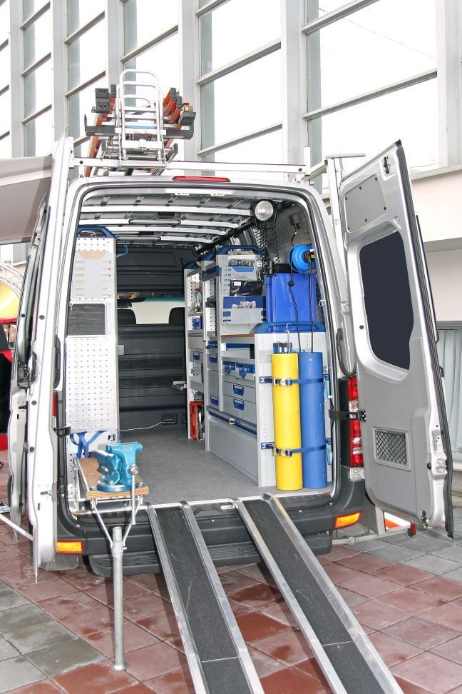 Open van with equipment and hoses inside, parked in a garage with ramps and tools.