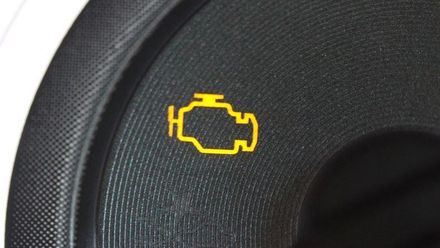 A yellow engine light is on the dashboard of a car.