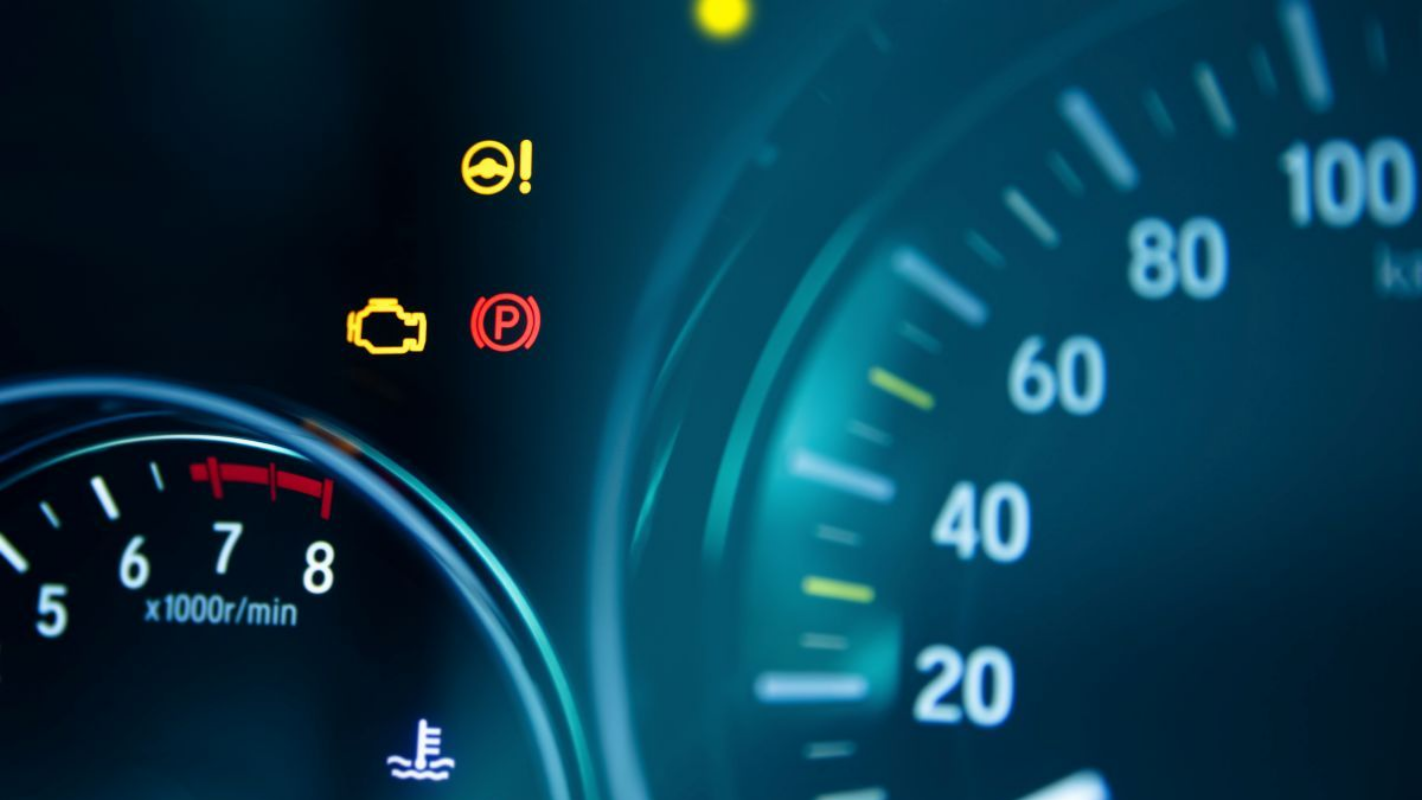 Car dashboard displaying illuminated warning icons, including the check engine light, parked brake, and power steering.