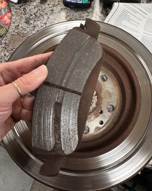 Worn brake pads held over a rusty brake rotor, showing heavy wear and groove marks