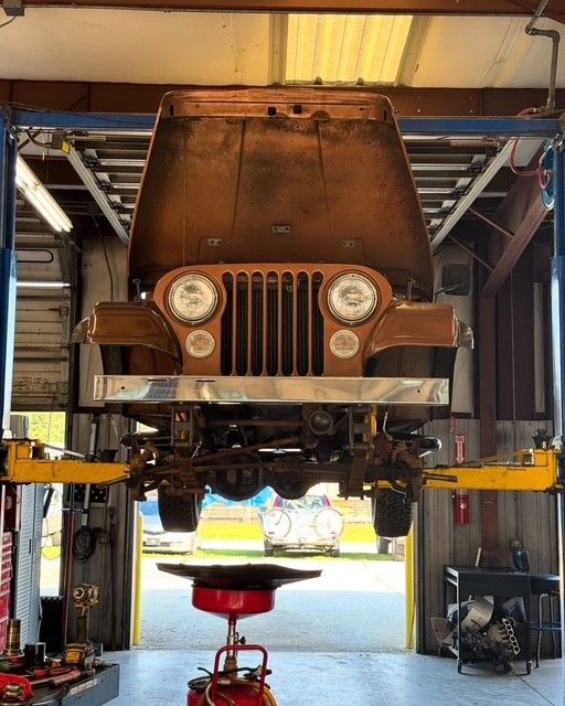 Rusty Jeep on a lift in an auto garage with the hood open and front end exposed