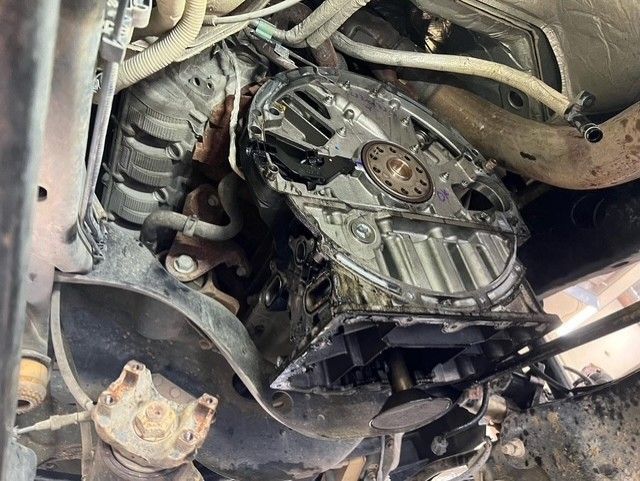 Broken vehicle transmission and drivetrain exposed under a car chassis, with damaged parts and debris.