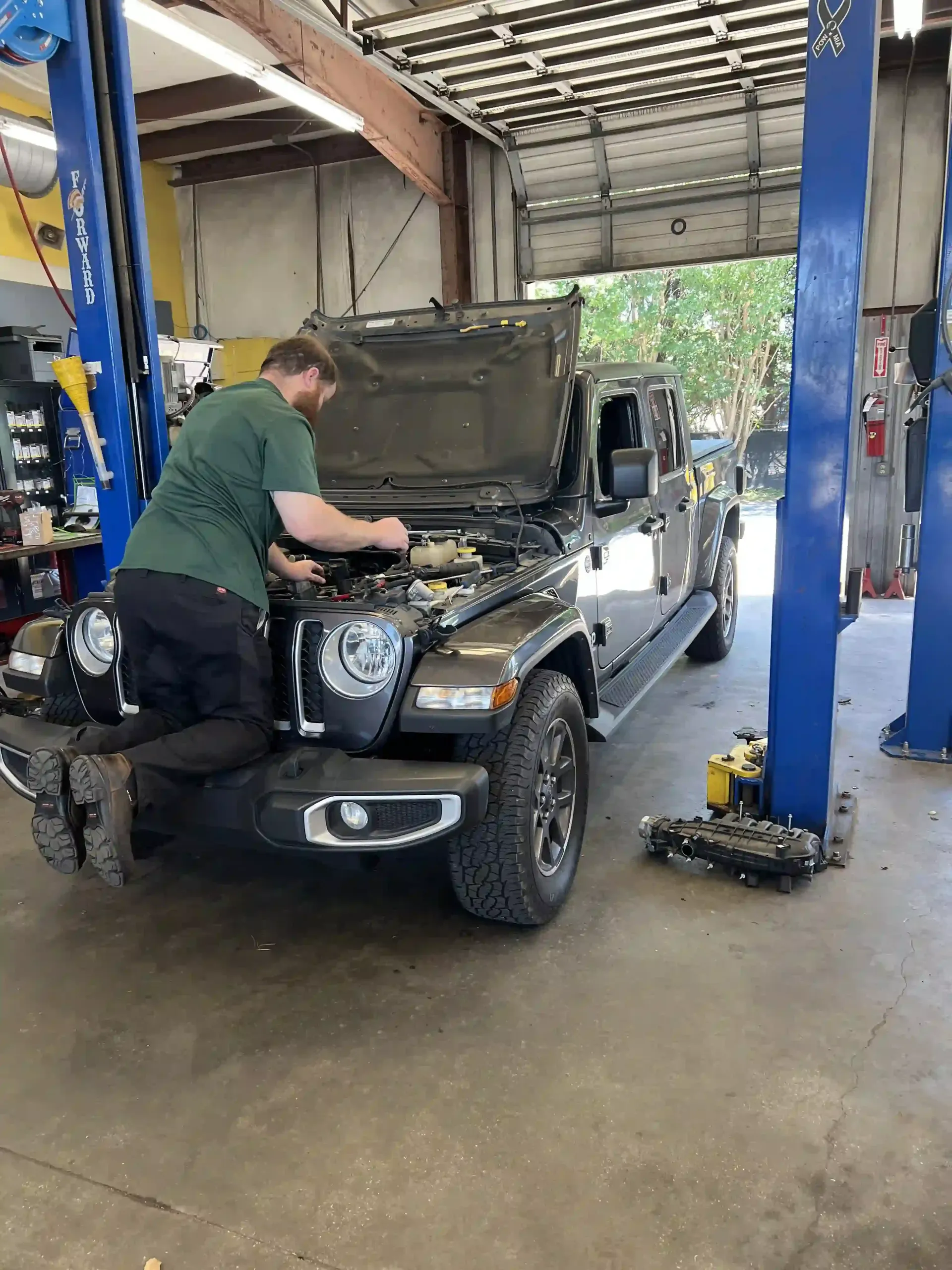 Mechanic working under an open-hood Jeep in a garage bay