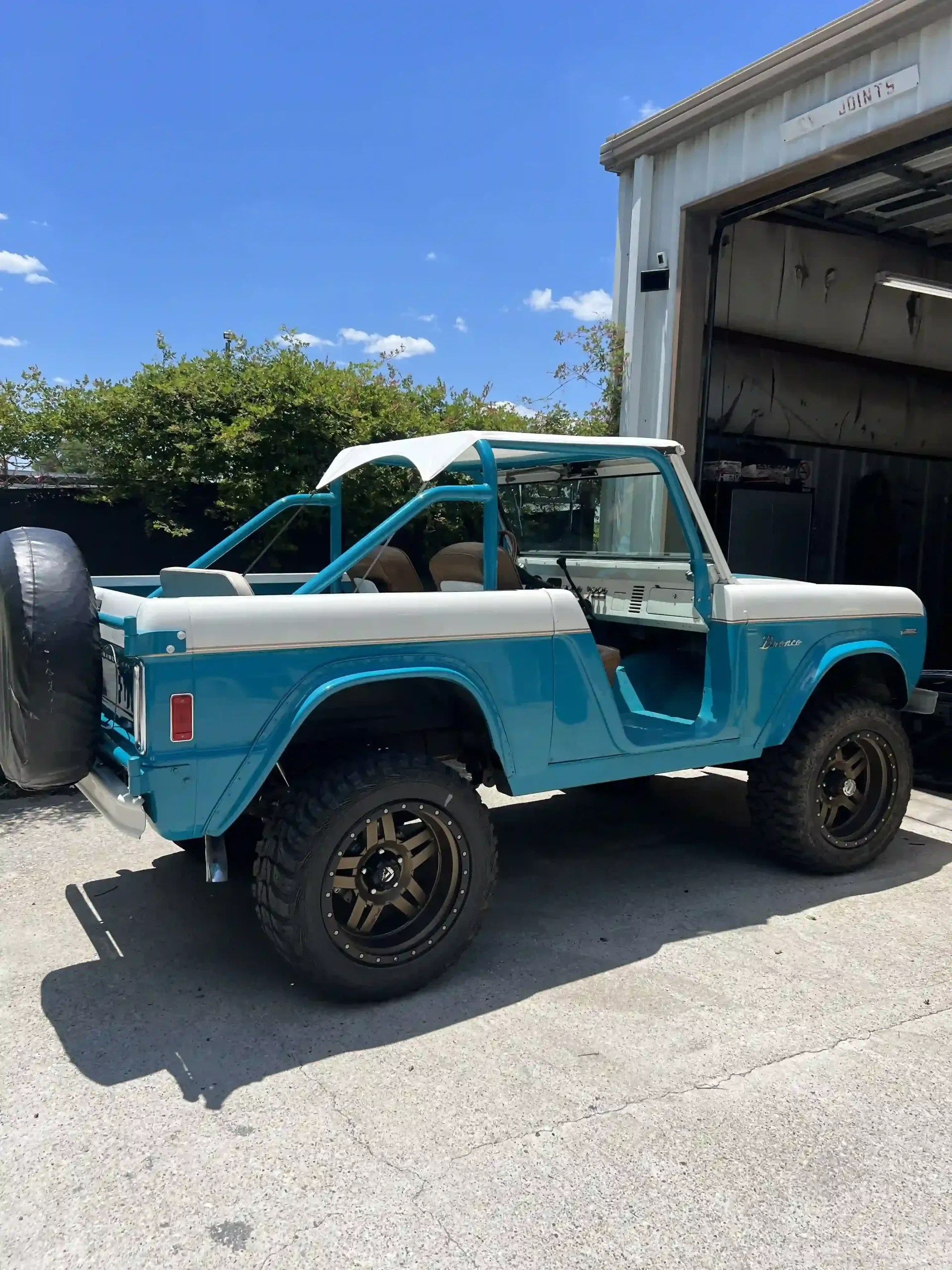 Blue vintage off-road truck parked outside a garage, with black wheels and a spare tire.