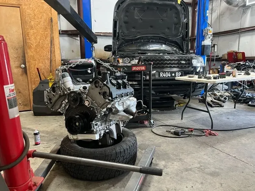 Car engine on a tire in a garage, with a black pickup truck and tools in the background