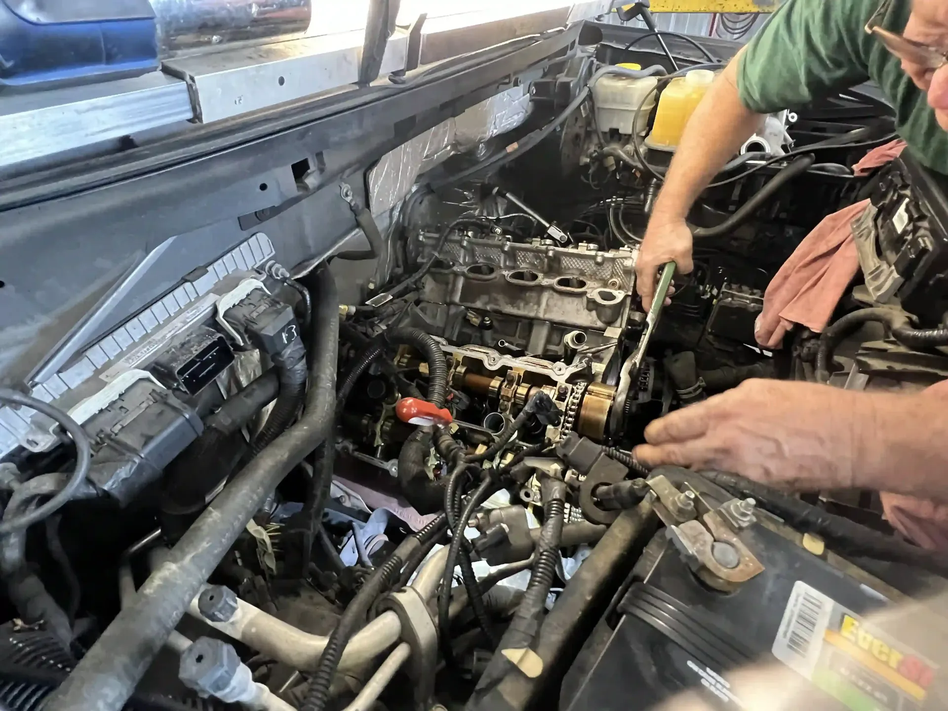Mechanic working under an open car hood in a garage, with tools and engine parts exposed