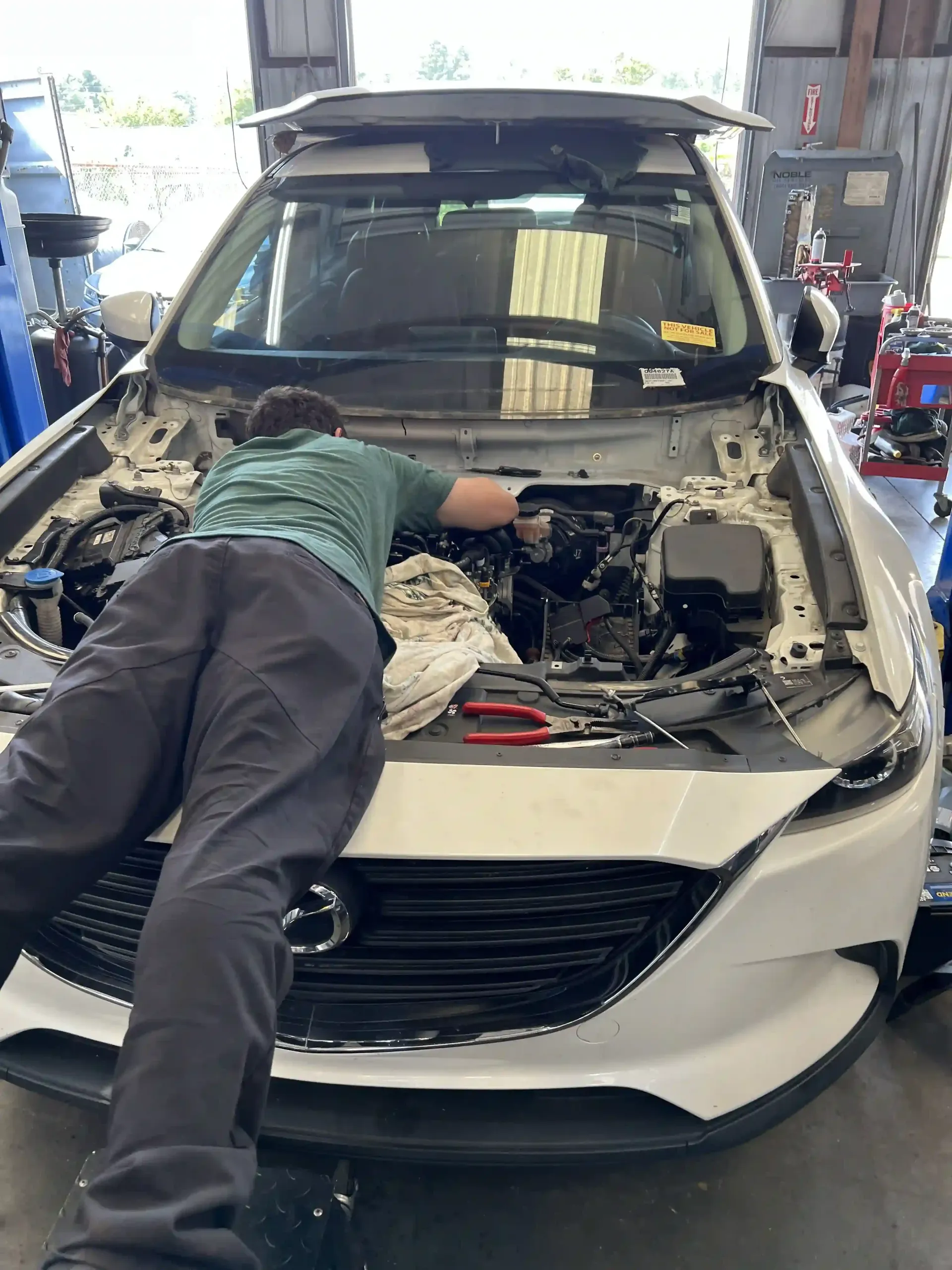 Mechanic leaning into the engine bay of a white car in a garage with the hood open.