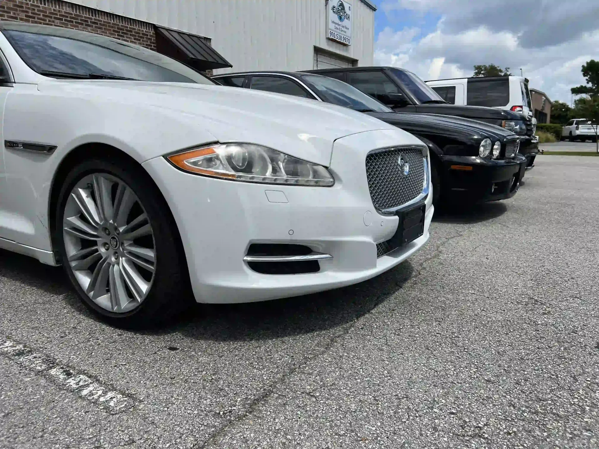 White sedan parked beside black car in a dealership lot on a cloudy day