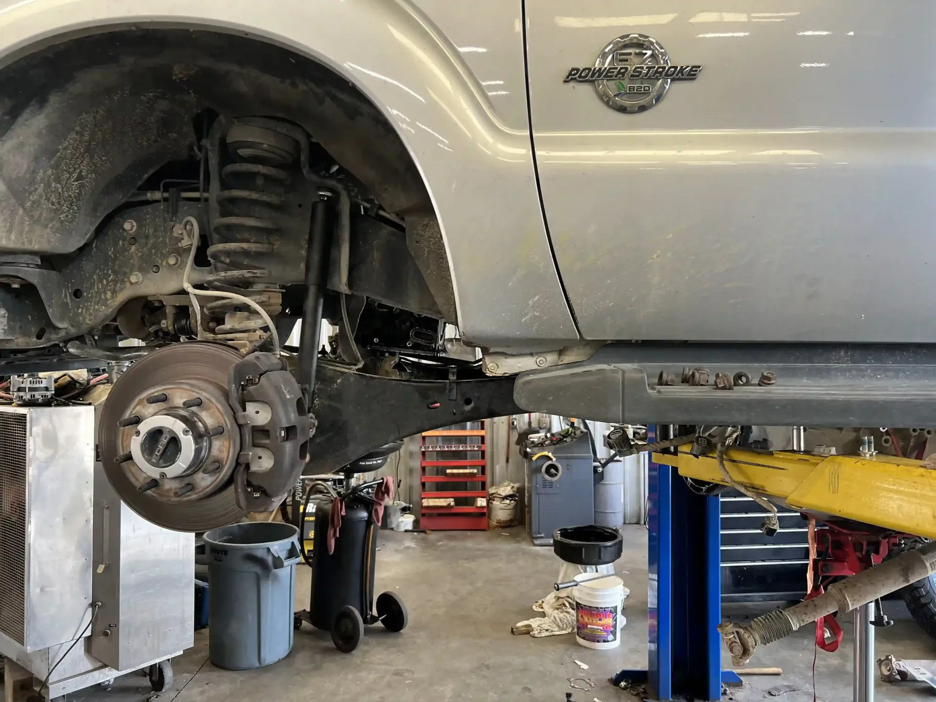 White SUV on a lift in an auto shop with the front wheel removed, exposing the brake and suspension.