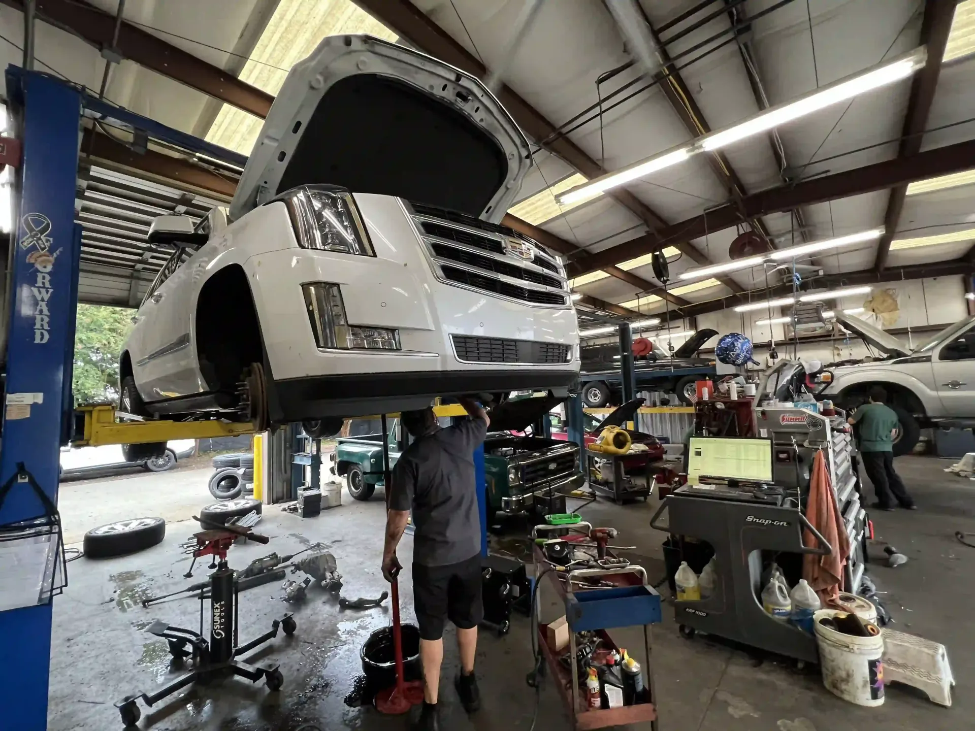 Car lifted in an auto repair shop, hood open, with tools and equipment scattered around.
