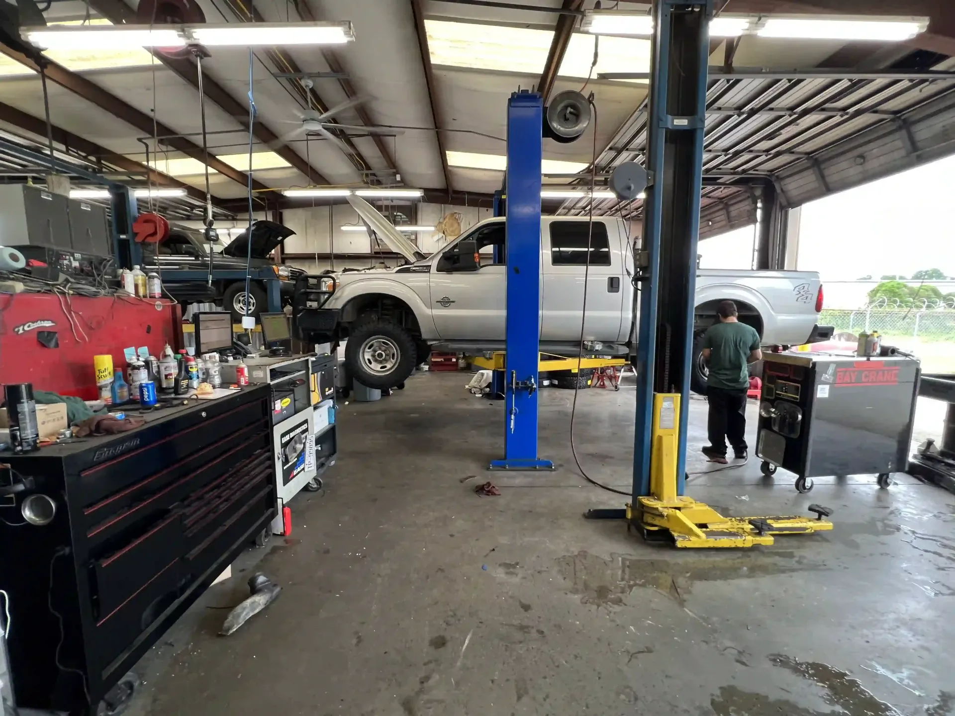 Auto repair shop with a white pickup on a lift, a mechanic, and tools in a garage bay