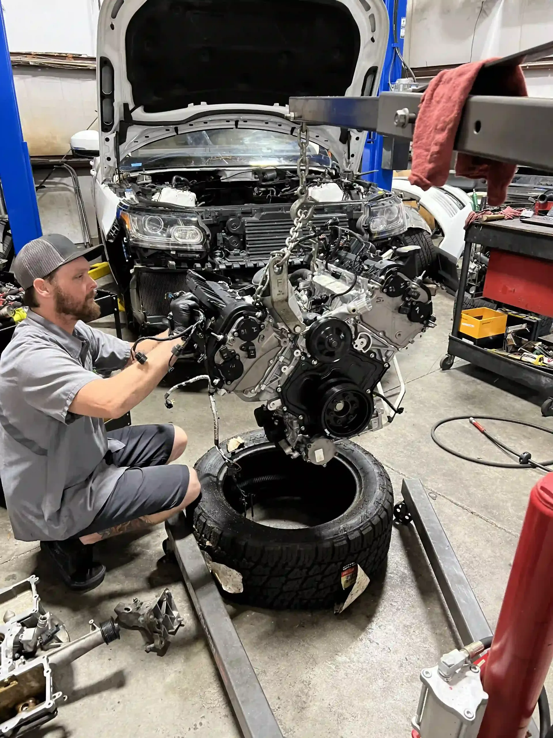 Mechanic removing a car engine in a garage, with the hood open and tools scattered nearby